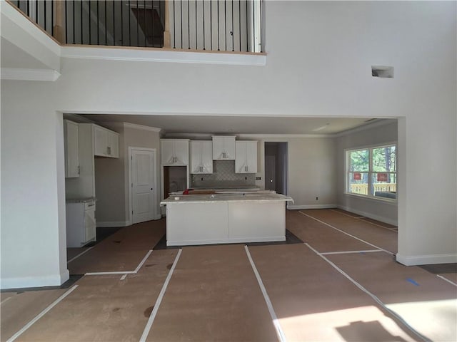 kitchen featuring a towering ceiling, white cabinets, ornamental molding, a center island, and tasteful backsplash