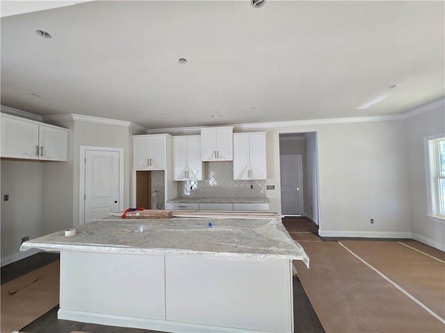 kitchen featuring baseboards, ornamental molding, a center island, white cabinetry, and backsplash