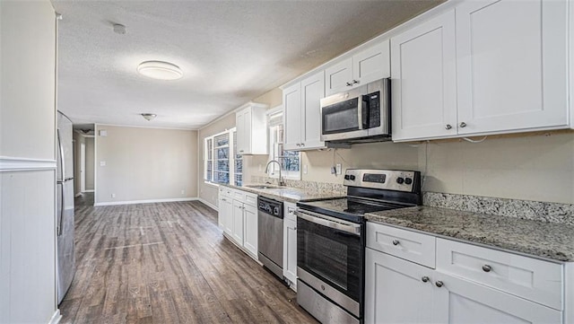 kitchen featuring dark wood-type flooring, light stone countertops, white cabinets, appliances with stainless steel finishes, and sink