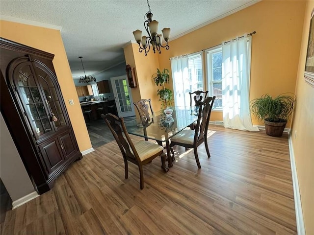 dining area with a textured ceiling, ornamental molding, wood-type flooring, and a chandelier