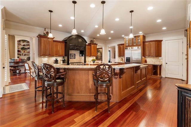 kitchen with built in fridge, light stone countertops, a breakfast bar area, and decorative light fixtures