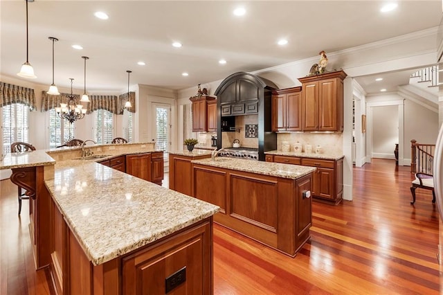 kitchen with a spacious island, light stone countertops, light wood-type flooring, and decorative light fixtures