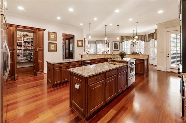 kitchen with a large island with sink, crown molding, pendant lighting, and dark hardwood / wood-style flooring