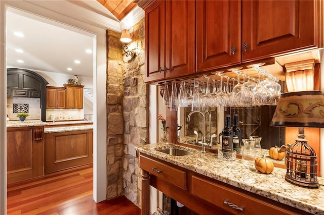 bar featuring wood-type flooring, sink, light stone counters, and decorative backsplash