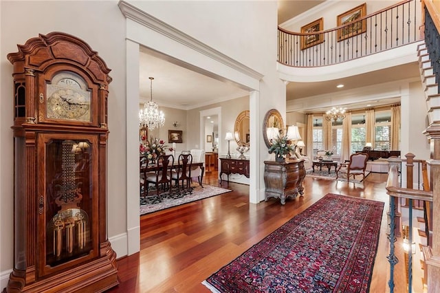 foyer with an inviting chandelier, hardwood / wood-style floors, a towering ceiling, and ornamental molding