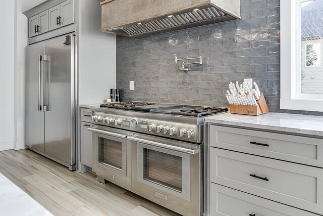 6014 Warpath Rd, Flowery Branch, GA 30542 - kitchen featuring high quality appliances, premium range hood, decorative backsplash, light stone countertops, and light wood-style flooring