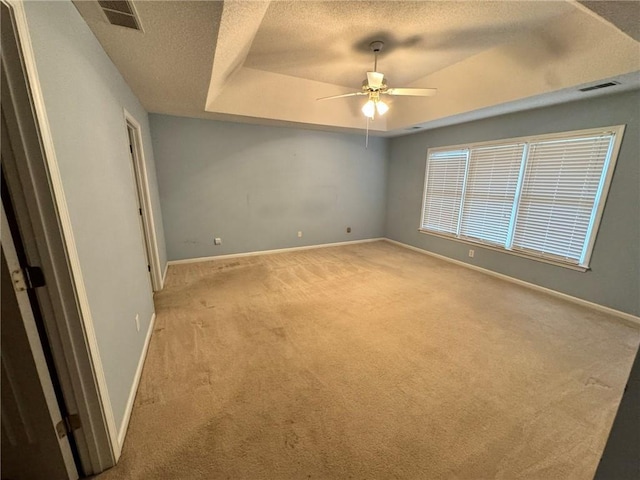 unfurnished bedroom featuring a textured ceiling, a tray ceiling, visible vents, and baseboards