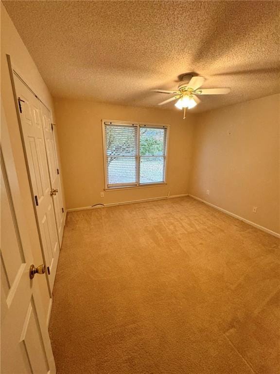 unfurnished bedroom featuring a textured ceiling, light carpet, a ceiling fan, baseboards, and a closet