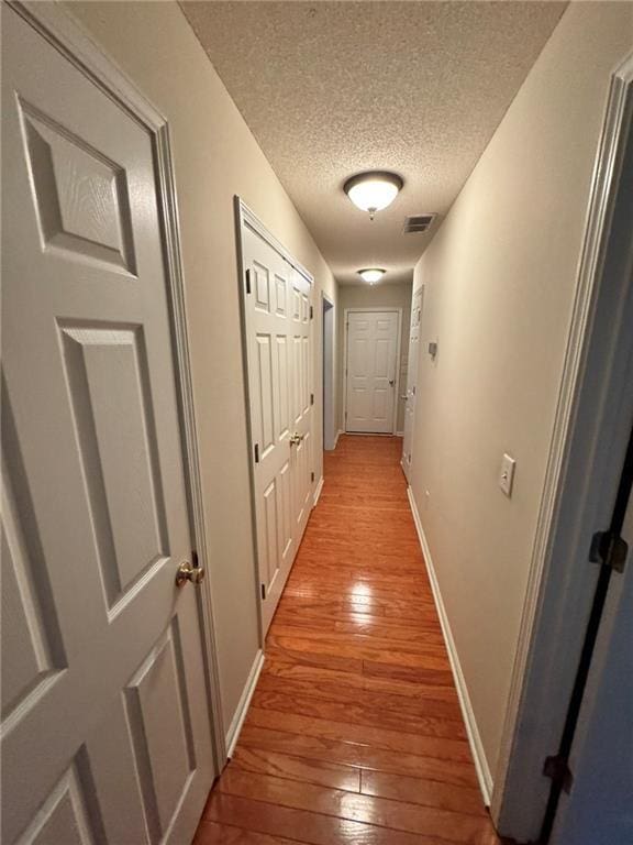 hallway featuring a textured ceiling, visible vents, hardwood / wood-style flooring, and baseboards