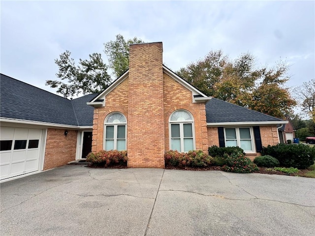 traditional-style home featuring a garage, brick siding, roof with shingles, and a chimney