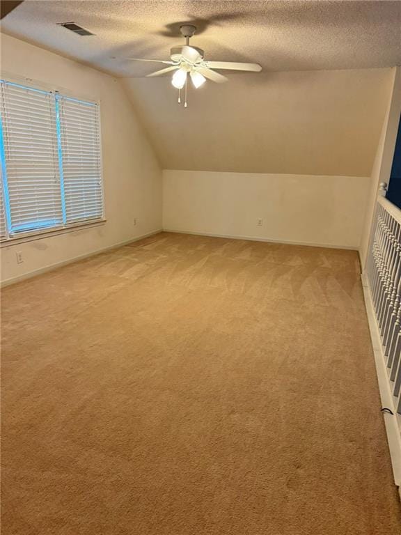 bonus room featuring visible vents, light colored carpet, vaulted ceiling, a textured ceiling, and ceiling fan