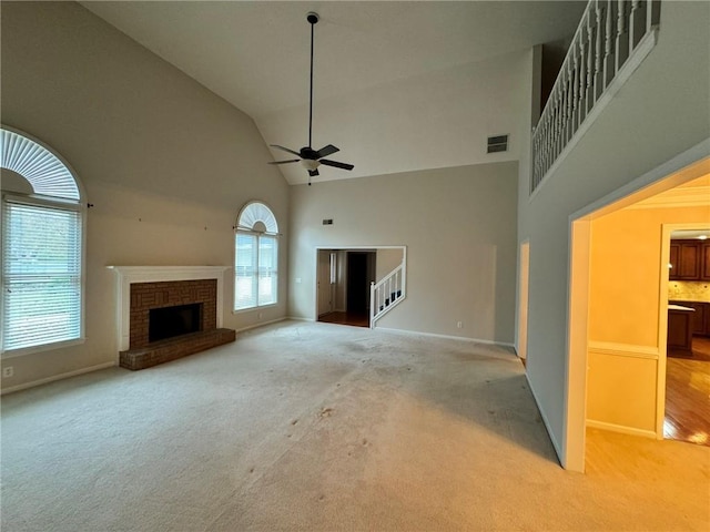 unfurnished living room with carpet floors, a fireplace, visible vents, a towering ceiling, and ceiling fan