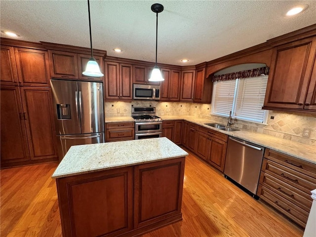 kitchen with a center island, light wood finished floors, appliances with stainless steel finishes, a sink, and light stone countertops