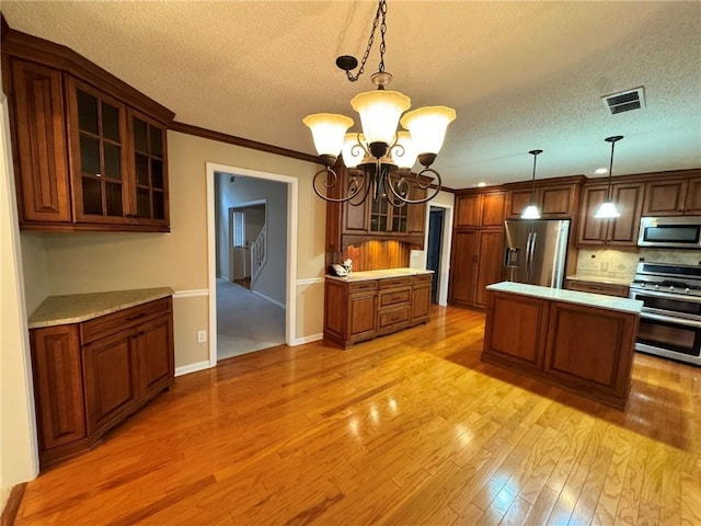 kitchen with light countertops, visible vents, appliances with stainless steel finishes, glass insert cabinets, and light wood-type flooring