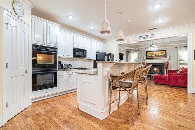725 Windsor Place Cir SW, Grayson, GA 30017 - kitchen with black appliances, crown molding, a kitchen breakfast bar, a lit fireplace, and light wood-style flooring