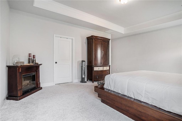 carpeted bedroom featuring baseboards, a raised ceiling, and a glass covered fireplace
