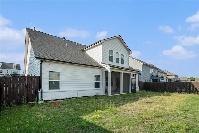 back of property featuring a lawn, a sunroom, brick siding, a fenced backyard, and a shingled roof