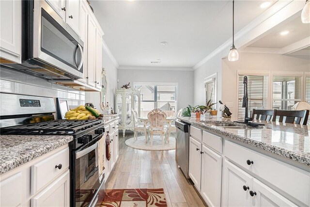 kitchen featuring white cabinets, a sink, light wood-style flooring, appliances with stainless steel finishes, and backsplash