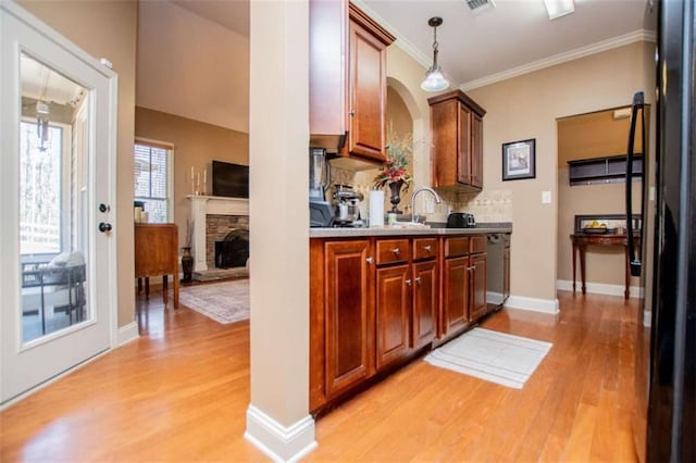 kitchen with light wood-type flooring, ornamental molding, a stone fireplace, a sink, and tasteful backsplash