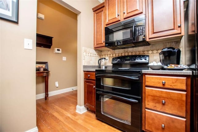 kitchen featuring baseboards, light wood finished floors, brown cabinets, black appliances, and tasteful backsplash