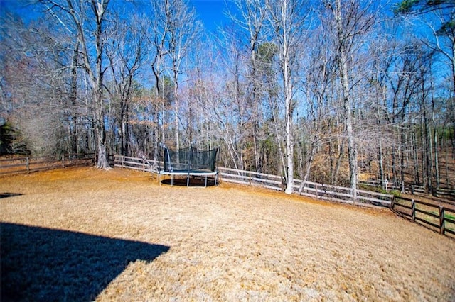 view of yard featuring a trampoline, fence, and a forest view