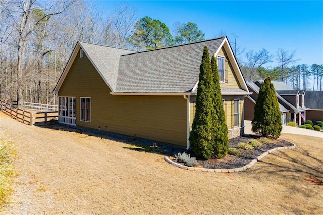 view of side of home featuring a shingled roof and fence