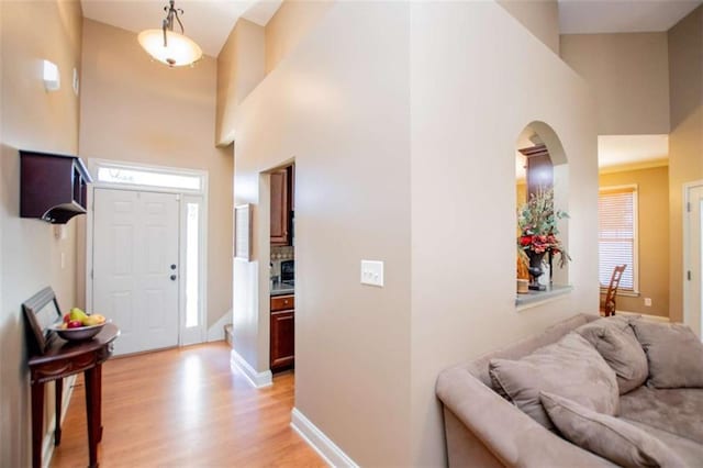 foyer entrance featuring light wood-type flooring, baseboards, a high ceiling, and arched walkways