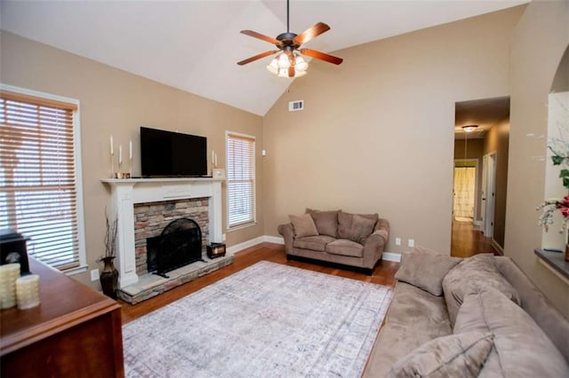 living room featuring a stone fireplace, wood finished floors, visible vents, and ceiling fan