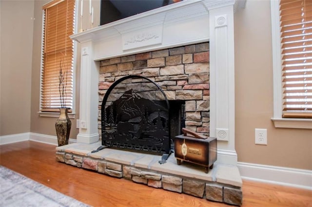 room details featuring baseboards, a stone fireplace, and wood finished floors