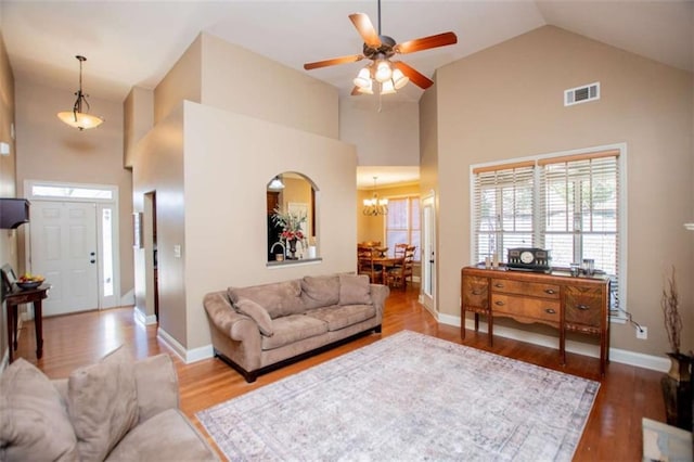 living room featuring visible vents, high vaulted ceiling, ceiling fan with notable chandelier, wood finished floors, and baseboards