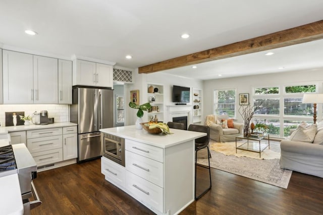kitchen with appliances with stainless steel finishes, beam ceiling, light countertops, white cabinetry, and open floor plan