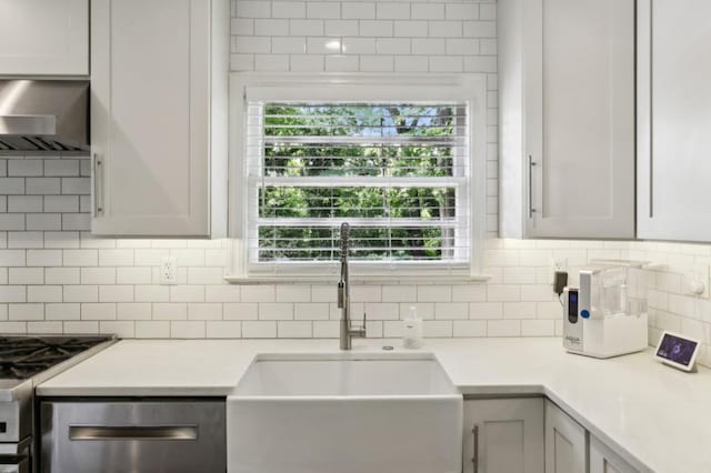 kitchen featuring appliances with stainless steel finishes, a sink, light countertops, wall chimney exhaust hood, and decorative backsplash