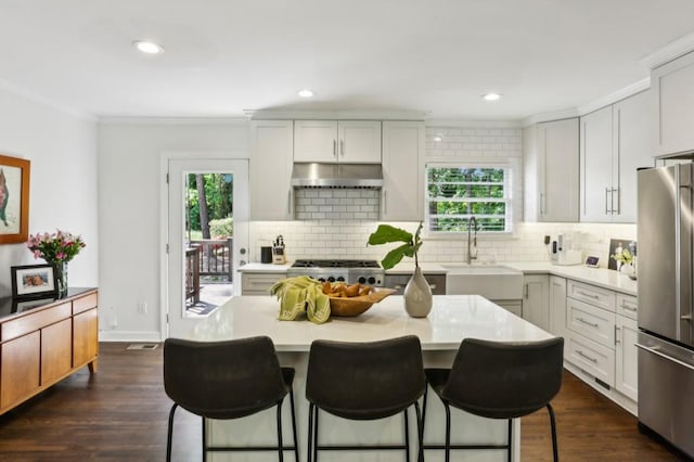 kitchen featuring a sink, freestanding refrigerator, a kitchen bar, under cabinet range hood, and ornamental molding
