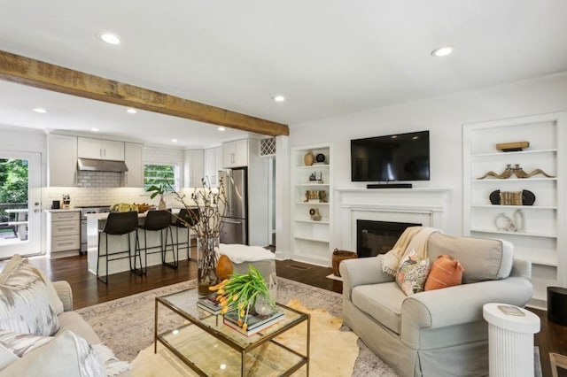 living room featuring dark wood-style flooring, a glass covered fireplace, beam ceiling, and a healthy amount of sunlight