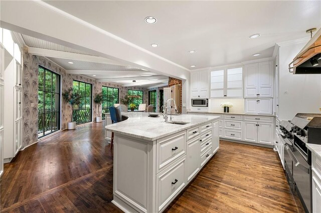 kitchen with an island with sink, sink, white cabinetry, light stone countertops, and stainless steel microwave