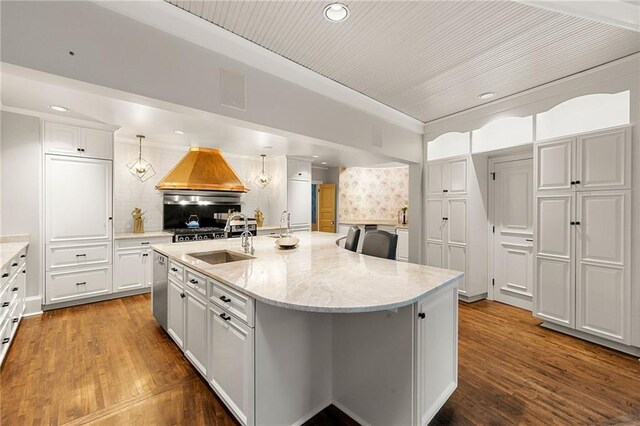 kitchen with white cabinets, sink, decorative light fixtures, a kitchen island with sink, and light wood-type flooring