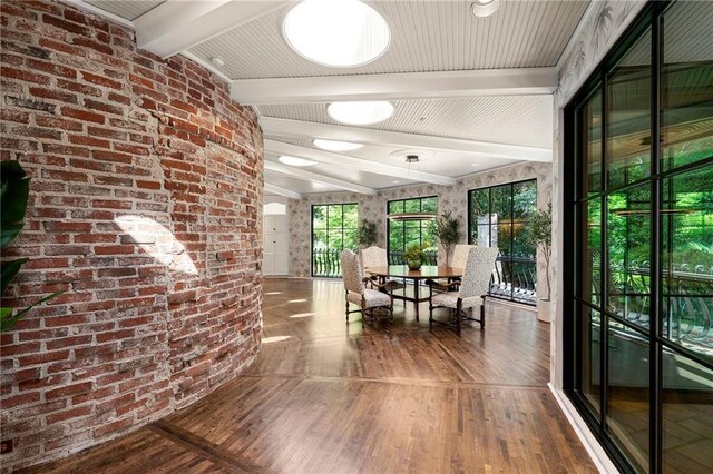 corridor with lofted ceiling with beams, wood-type flooring, and brick wall