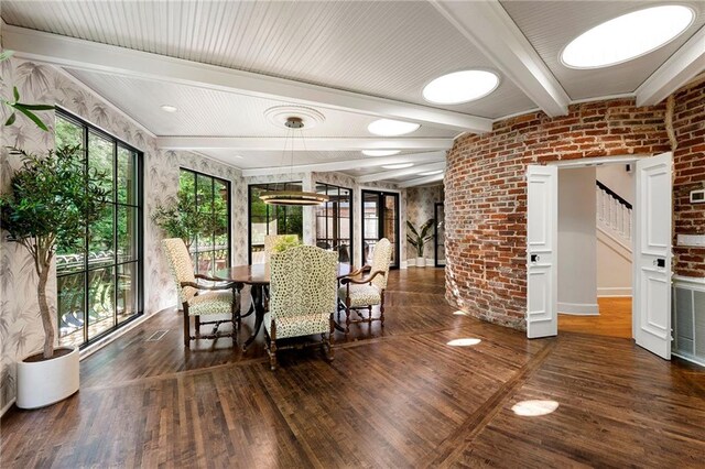 unfurnished dining area with dark hardwood / wood-style flooring, beamed ceiling, and brick wall