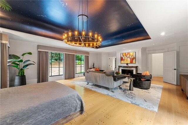 bedroom featuring light wood-type flooring, a tray ceiling, a chandelier, a premium fireplace, and crown molding