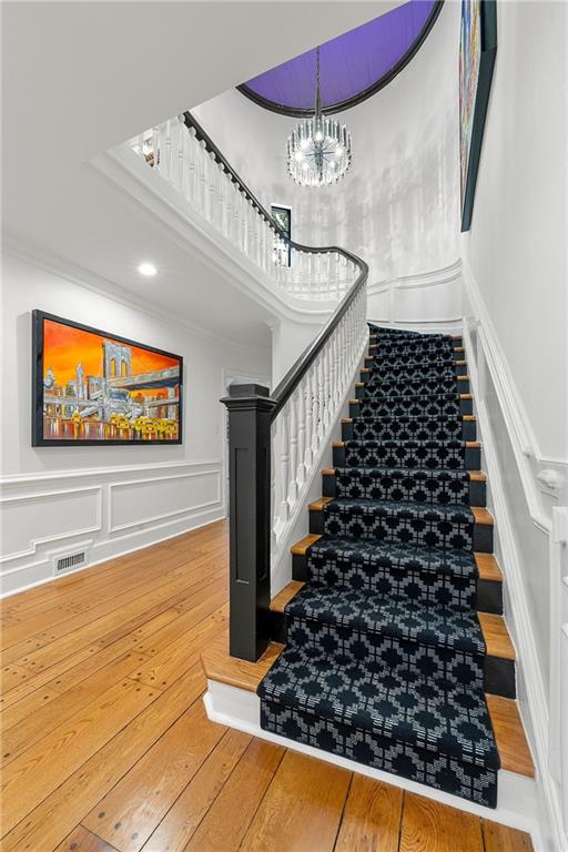 staircase featuring wood-type flooring, an inviting chandelier, and crown molding