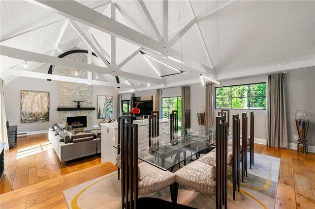 dining area with high vaulted ceiling, beam ceiling, light hardwood / wood-style floors, and a fireplace