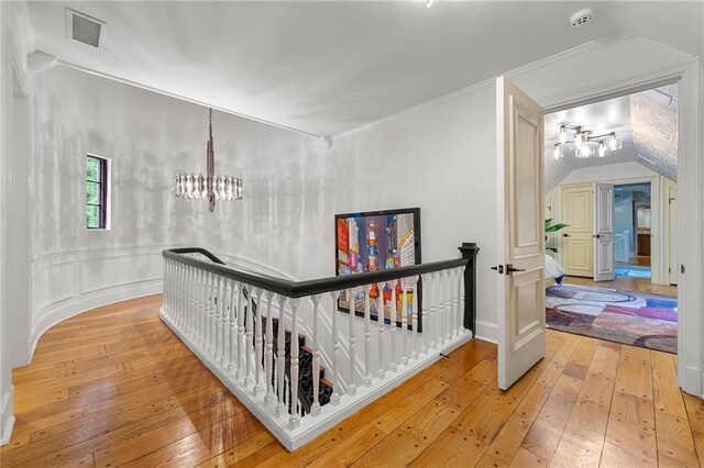 hallway with crown molding, lofted ceiling, light hardwood / wood-style flooring, and a chandelier