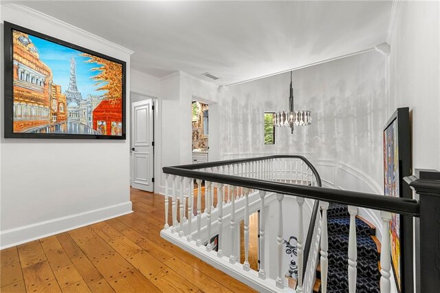 staircase featuring wood-type flooring, ornamental molding, and a chandelier