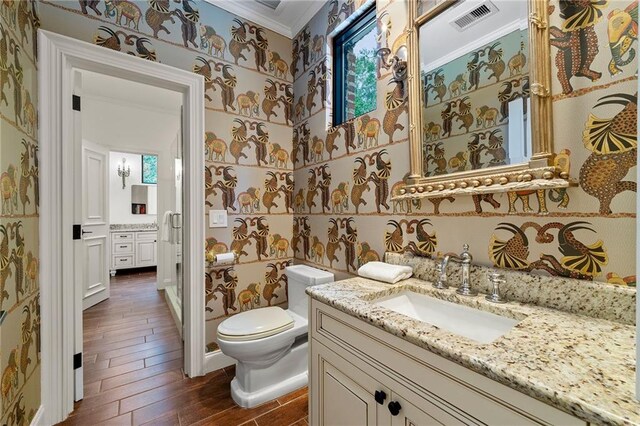 bathroom featuring vanity, wood-type flooring, crown molding, toilet, and a healthy amount of sunlight