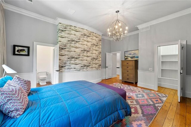 bedroom featuring wood-type flooring, an inviting chandelier, a walk in closet, ensuite bathroom, and crown molding