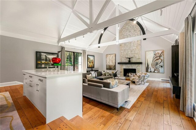 living room featuring light wood-type flooring, track lighting, beam ceiling, a fireplace, and high vaulted ceiling