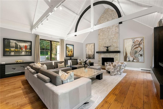 living room featuring track lighting, beam ceiling, a fireplace, light hardwood / wood-style flooring, and high vaulted ceiling