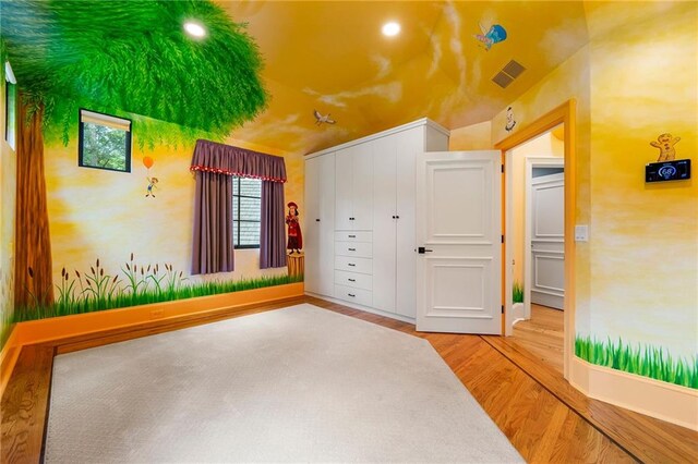 unfurnished bedroom with wood-type flooring, lofted ceiling, and a closet