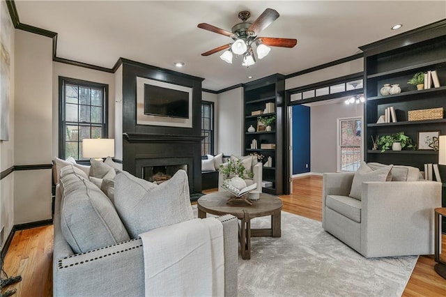 living area featuring a fireplace, wood finished floors, a ceiling fan, baseboards, and crown molding