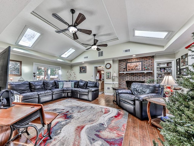 living room featuring dark hardwood / wood-style flooring, built in shelves, ceiling fan, lofted ceiling with skylight, and a fireplace